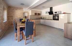 A modern kitchen with white cabinets, a black oven, and a dining area with a glass table and chairs. - Gorgeous home in Rovinjsko Selo with WiFi (Rovinjsko Selo)
