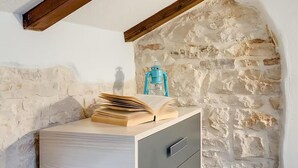 Una habitación con pared de piedra, techo con vigas de madera, un escritorio con cajones y un farol azul.