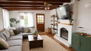 Een woonkamer met een bank, salontafel, open haard, televisie en decoratieve planten.