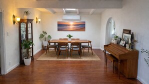 Een eetruimte met een houten tafel en stoelen, een schilderij erboven en een piano aan de rechterkant.