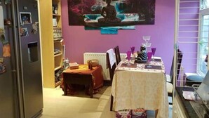 Ein Essbereich mit einem Tisch für zwei Personen, einem Kühlschrank und einer violetten Wand mit einem großen Gemälde.