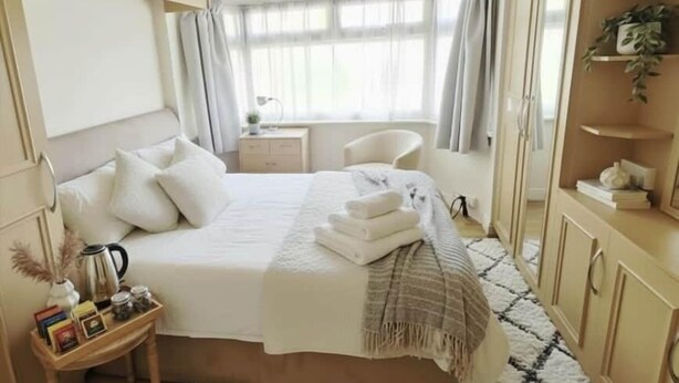 Ein Schlafzimmer mit Bett, Nachttisch, Stuhl, Kleiderschrank und einem Fenster mit Vorhängen.