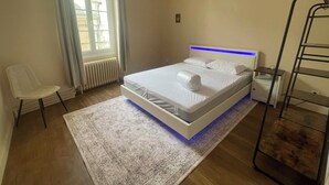 A modern bedroom with a bed, a chair, a radiator, and a window with curtains. - 3-bedroom apartment in the heart of the Alpes Mancelles, 20 minutes from the 24h of Le Mans (Beaumont-sur-Sarthe)