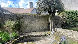 A stone well with a Buddha statue, surrounded by greenery and a stone wall. - 3-bedroom apartment in the heart of the Alpes Mancelles, 20 minutes from the 24h of Le Mans (Beaumont-sur-Sarthe)