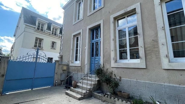 A two-story building with a blue door, a gated entrance, and a small set of stairs leading to the entrance. - 3-bedroom apartment in the heart of the Alpes Mancelles, 20 minutes from the 24h of Le Mans (Beaumont-sur-Sarthe)