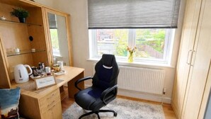 Een kleine kamer met een bureau, stoel en raam met jaloezieën.