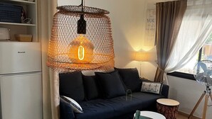 A cozy living room with a dining table set for two, a sofa, a ceiling fan, and a kitchen area with a refrigerator. - Susana - cozy  1-bedroom apartment in charming Corralejo perfect for relaxing (Corralejo)