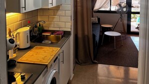 A compact kitchen with a microwave, toaster, and washing machine. A small dining area with a table and chair is visible through a window. - Susana - cozy  1-bedroom apartment in charming Corralejo perfect for relaxing (Corralejo)