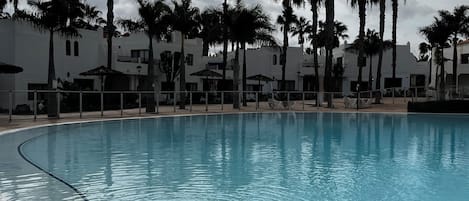 Una piscina con bordes de azulejos, rodeada de palmeras y edificios blancos.