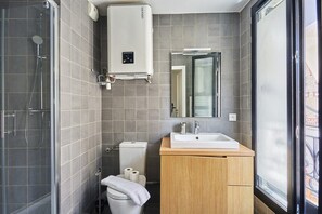 A modern bathroom with a glass shower enclosure, a toilet, a sink with a mirror above it, and a window providing a view of the outside. - Charming Apartement Boulogne Billancourt Center (Boulogne-Billancourt)