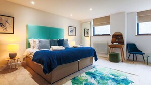 A modern bedroom with a bed, bedside lamps, a desk, a chair, and artwork on the walls. - Boutique King Suite - Penarth (Vale of Glamorgan)