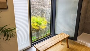 A room with a wooden bench, a window with blinds, a stone wall, and a tiled floor. - Boutique King Suite - Penarth (Vale of Glamorgan)