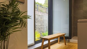 A room with a wooden bench, a potted plant, a stone wall, and a view through a glass door. - Boutique King Suite - Penarth (Vale of Glamorgan)