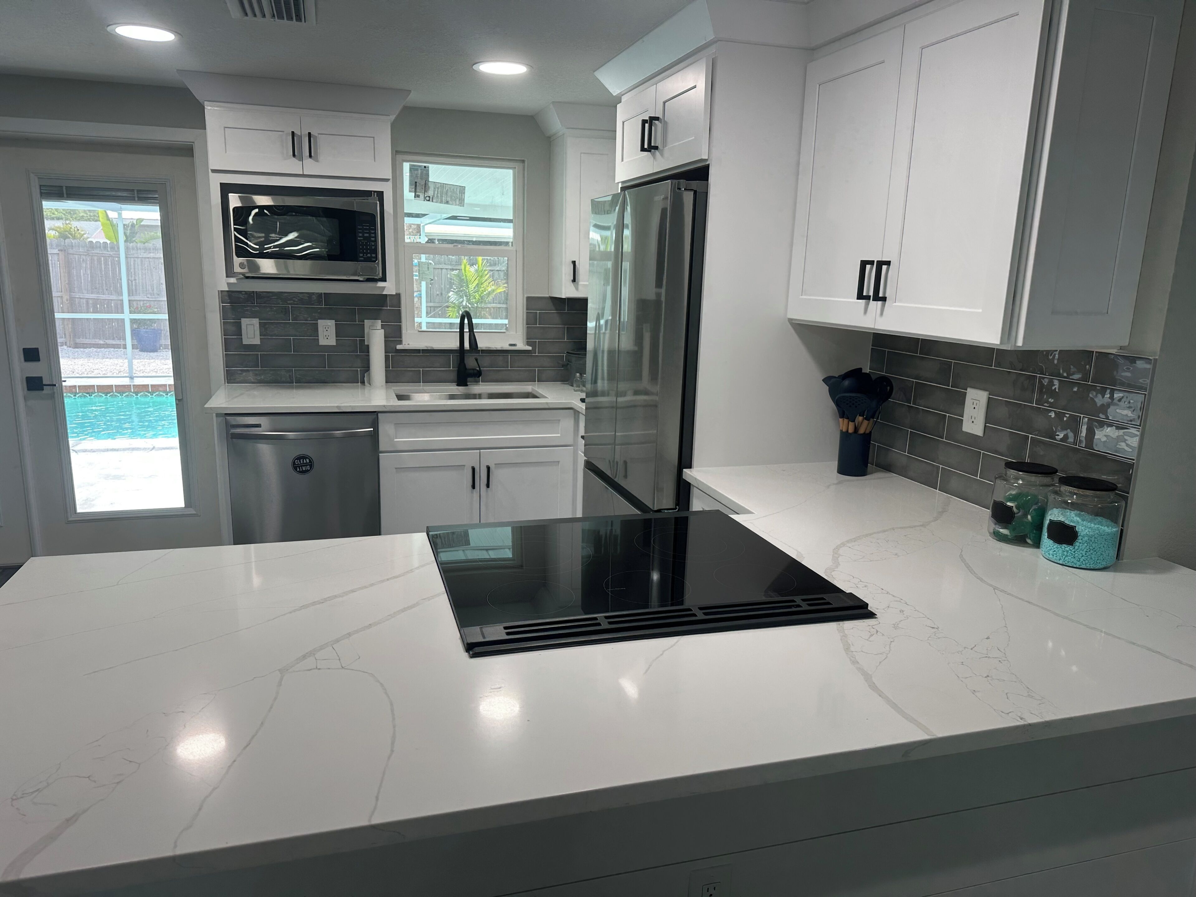 A modern kitchen with white cabinets, a stainless steel refrigerator, a built-in microwave, and a black induction cooktop.