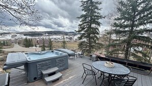 Una terraza con jacuzzi, mobiliario exterior y vista a un paisaje nevado.