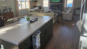 Una cocina moderna con una isla grande, un comedor con mesa y sillas, una sala de estar con sofá y televisor, y una chimenea.