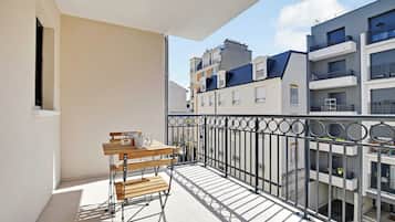 Un balcón con mesa y sillas de madera, barandilla de metal y vistas a edificios cercanos.