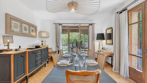 Ein Esszimmer mit einem langen Tisch, gedeckt für sechs Personen, einer Chandelierleuchtre und Blick ins Freie.