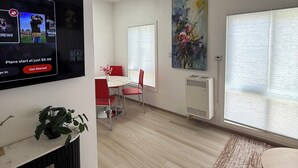 A modern living room with a flat-screen TV, a dining area with red chairs, a large window with blinds, and a painting on the wall. - Elegant Monet Studio Apartment (Los Angeles)