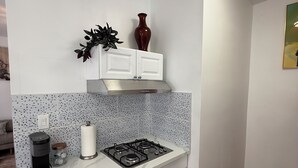 A kitchen with white cabinets, a gas stove, a coffee maker, and a decorative plant. - Elegant Monet Studio Apartment (Los Angeles)