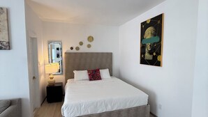 A bedroom with a bed, a nightstand, a lamp, a mirror, and a painting on the wall. - Elegant Monet Studio Apartment (Los Angeles)
