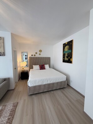 Ein Schlafzimmer mit Bett, Nachttisch, Lampe, Spiegel und einem Bild an der Wand.