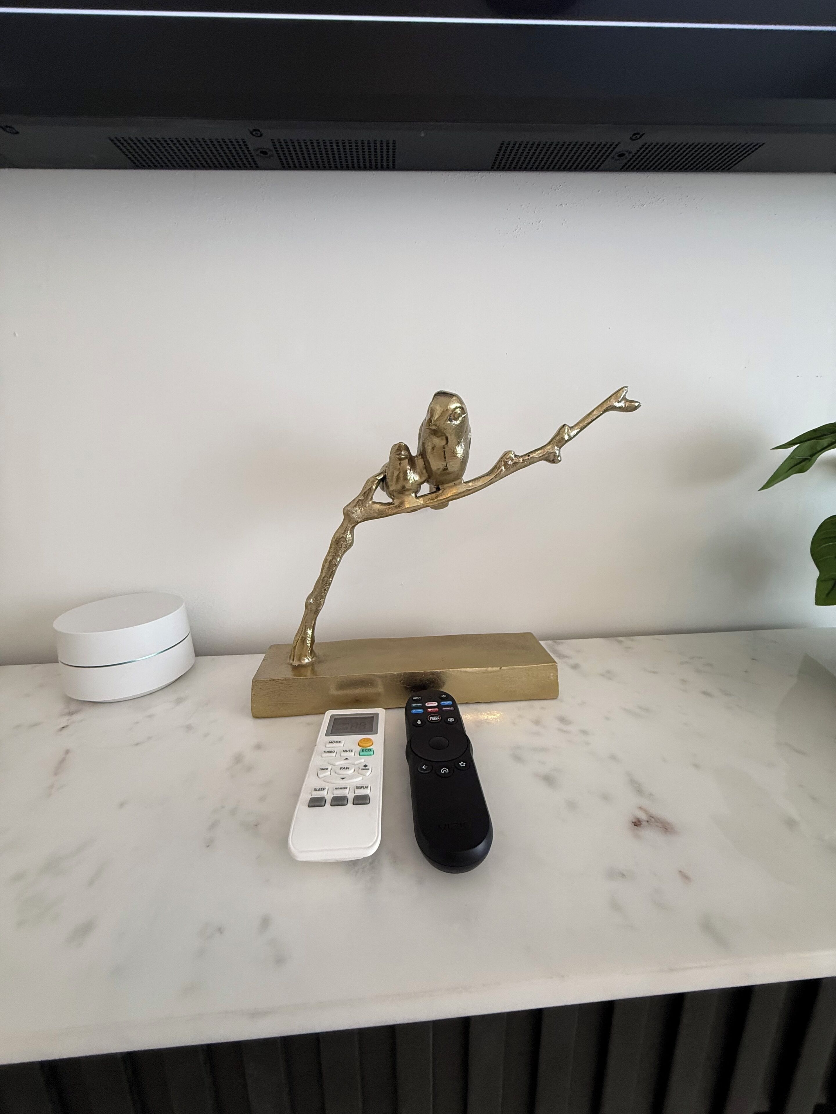 A marble countertop with a white speaker, a black remote, and a gold decorative piece.