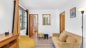 A hallway with a wooden floor, a yellow chair, a beige sofa, a small table, and a mirror on the wall. - Le Domaines Des Thermes – T2 with Shared Pool, Peaceful Setting, Mountain View (Gap)