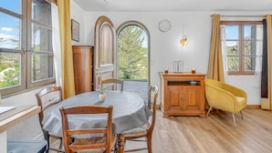 A dining area with a round table, chairs, a wooden cabinet, and a yellow armchair. - Le Domaines Des Thermes – T2 with Shared Pool, Peaceful Setting, Mountain View (Gap)