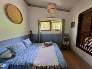 Ein Zimmer mit einem Bett, einem Vorhangfenster, einem Wandventilator und einer Wandklimaanlage.