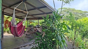 A covered outdoor area with a hammock, wooden deck, and lush greenery. - Maison Ylang avec Bungalow Uturoa (Raiatea)