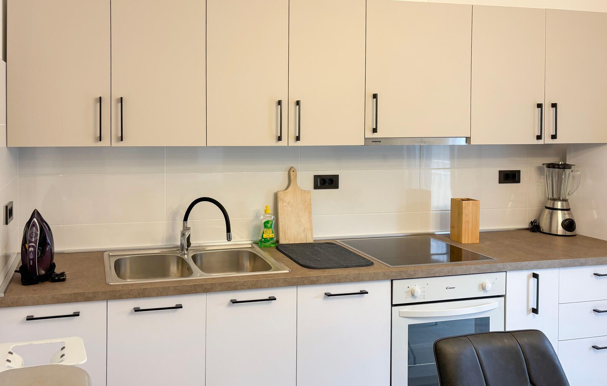 A kitchen with two sinks, a toaster, a blender, and a wooden cutting board.