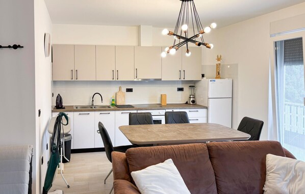 A modern kitchen with white cabinets, a dining table, and a brown sofa.