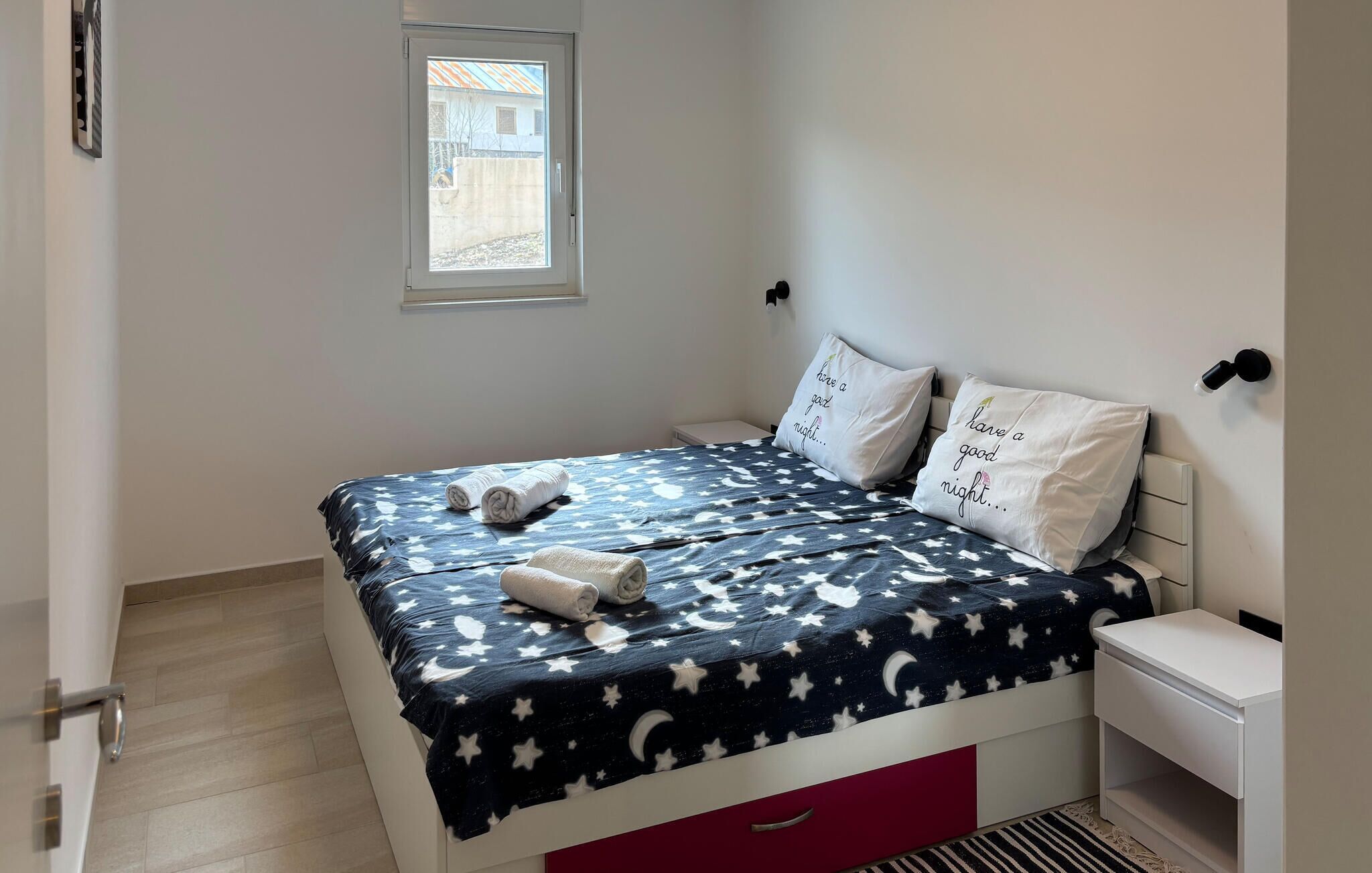 Una camera da letto con un letto, cuscini, un comodino e una finestra.