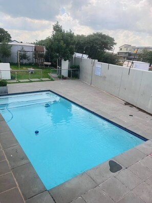 A rectangular swimming pool with a tiled edge, surrounded by a concrete deck.