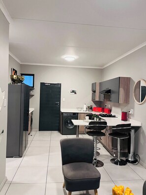A compact kitchen with a washing machine, a dining area with a chair, and a small table.