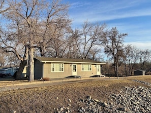 A single-story house with a front porch, a garage, and a yard with a stone border.