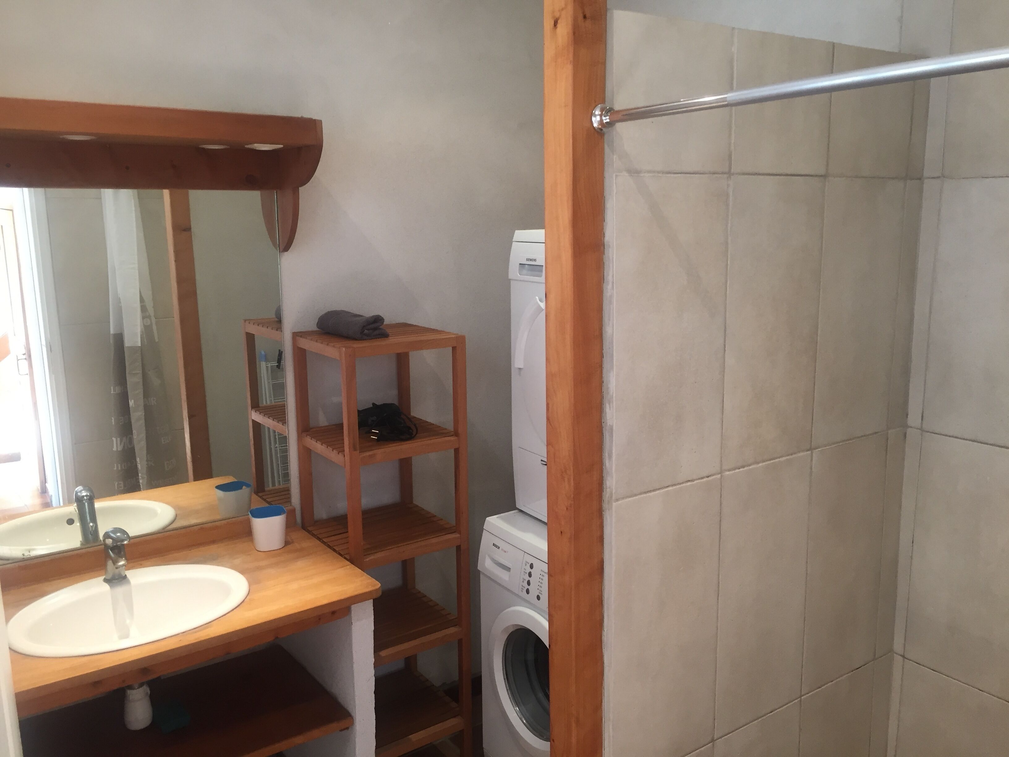 A bathroom with a wooden vanity, a sink, a mirror, a shelf with a towel, and a washing machine.