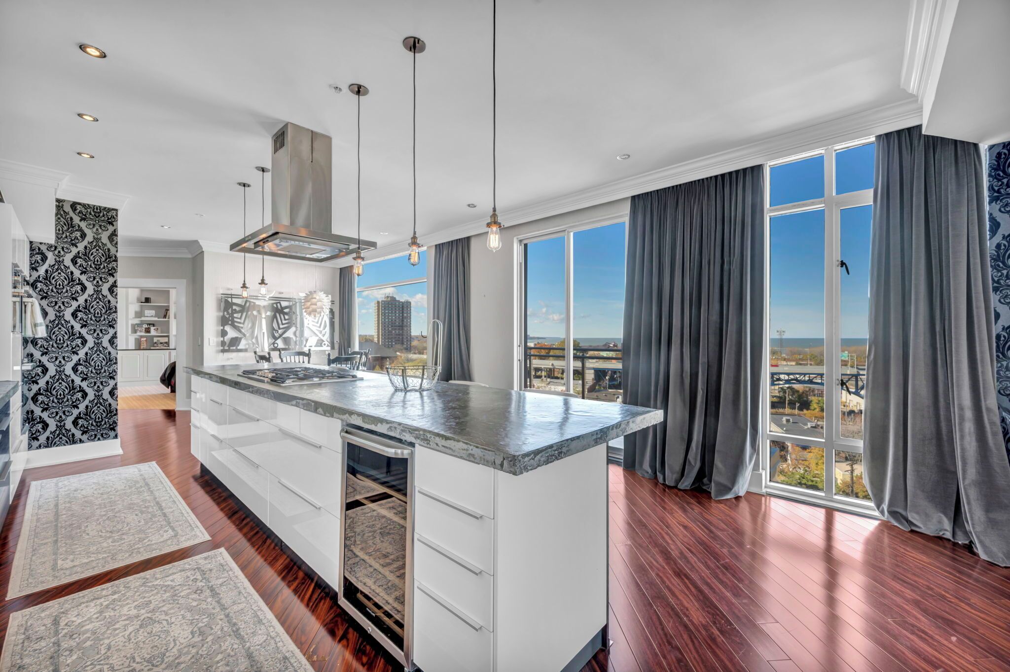A modern kitchen with a large island, pendant lighting, and a city view through large windows.