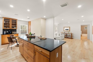 A modern kitchen with wooden cabinets, a black countertop, and a dining area with a white sofa and wooden side table. - Modern Waterfront, Private Ensuite Baths & Decks (Fairhope)