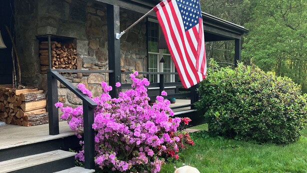 A stone house with a porch, a flag, and a dog. - Farmhouse on a River (South Kingstown)