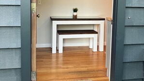 A room with a wooden floor, a white bench, a small table with a plant, and a painting on the wall. - Farmhouse on a River (South Kingstown)