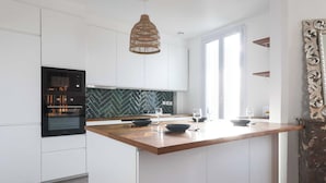 A modern kitchen with white cabinetry, a herringbone backsplash, a wooden island, and a hanging pendant light. - Magnificent Apartment -2br-6p- Saint-denis (Saint-Denis)