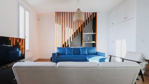 A modern living room with a blue sofa, a grey couch, a TV, and a staircase with striped walls. - Magnificent Apartment -2br-6p- Saint-denis (Saint-Denis)