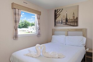 Una habitación de hotel con cama, ventana con cortinas, un cuadro de un paisaje urbano y una mesita de noche.