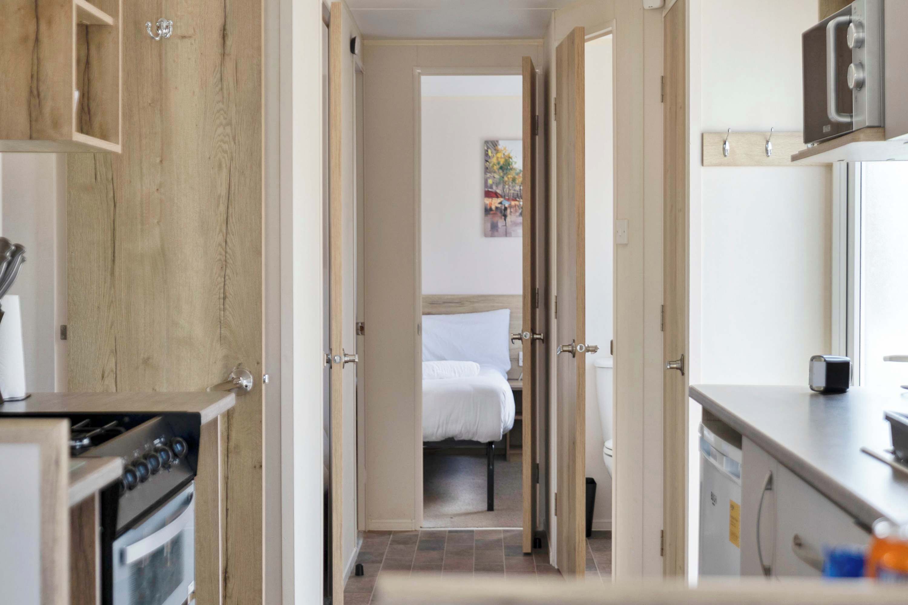 A narrow hallway leading to a bedroom with a bed, a kitchen area with a stove, and a bathroom with a toilet.