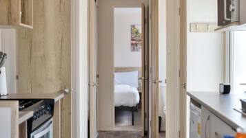 A narrow hallway leading to a bedroom with a bed, a kitchen area with a stove, and a bathroom with a toilet.