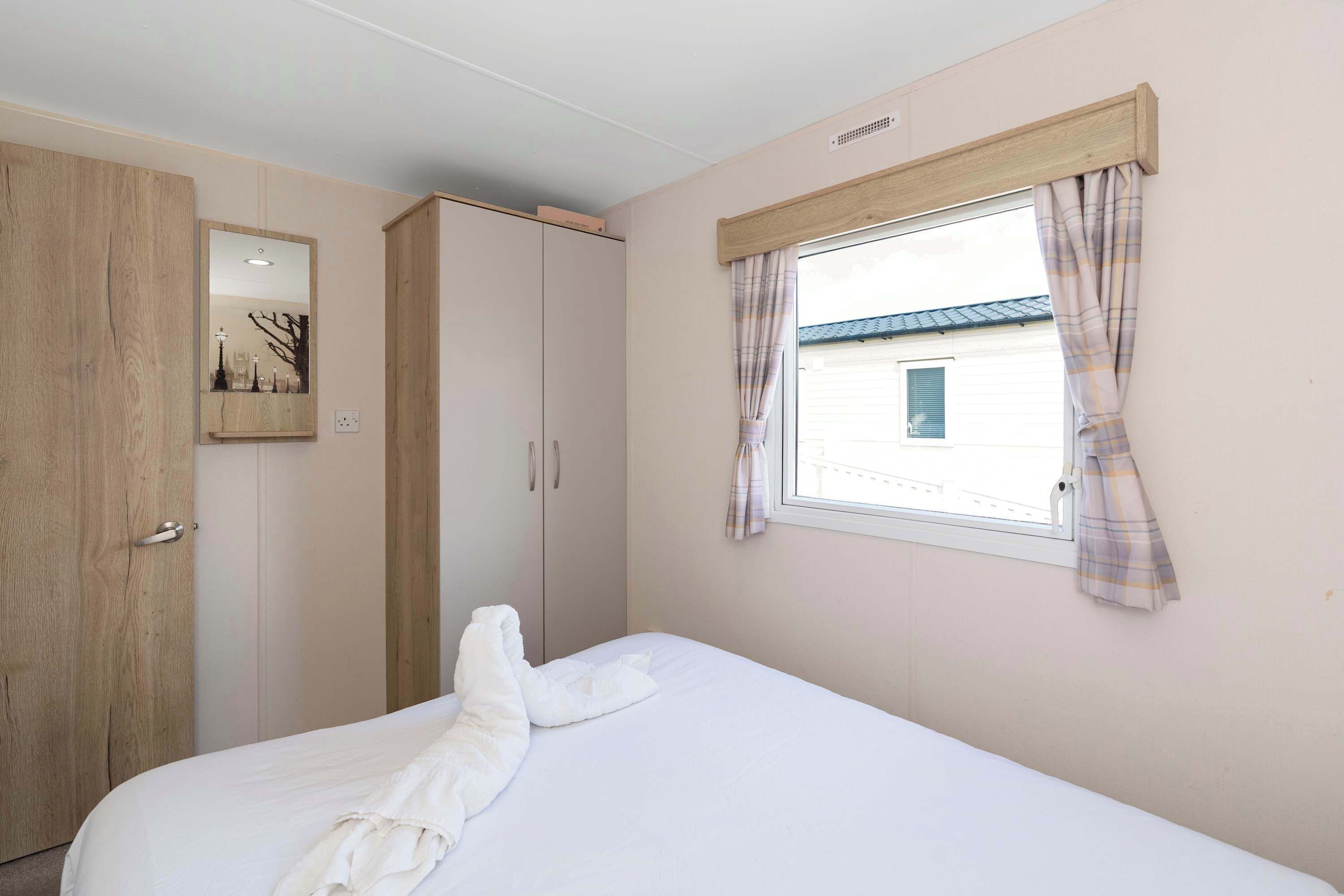 Een slaapkamer met een bed, een kledingkast, een raam met gordijnen en een spiegel.