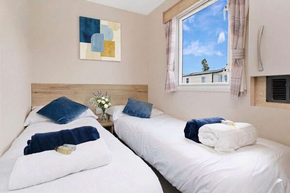 Ein Hotelzimmer mit zwei Betten, einem Holzkopfende, einem Fenster mit Vorhängen und einem Bild an der Wand.