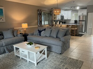 Ein modernes Wohnzimmer mit grauem Sofagarnitur, einem weißen Couchtisch und einem gemusterten Teppich.